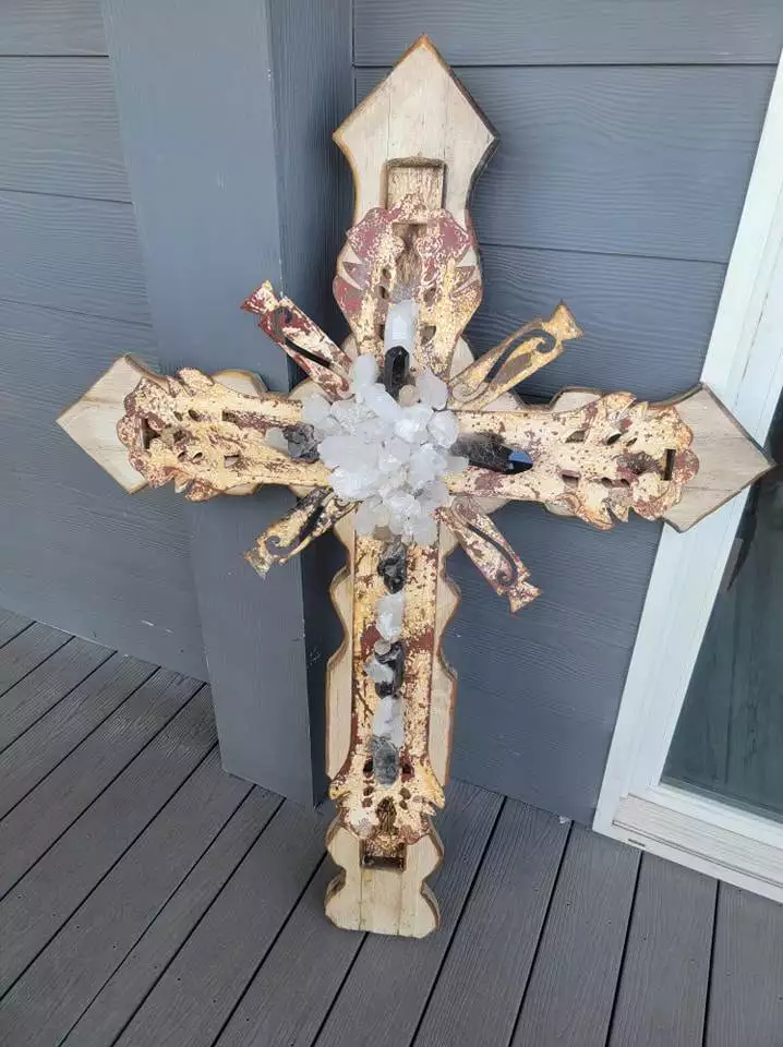 A beautifully crafted rustic wooden cross with Native American decorative elements and crystal accents from Red Coyote Trading Post rests against a gray wall in Ft. Mohave, AZ.