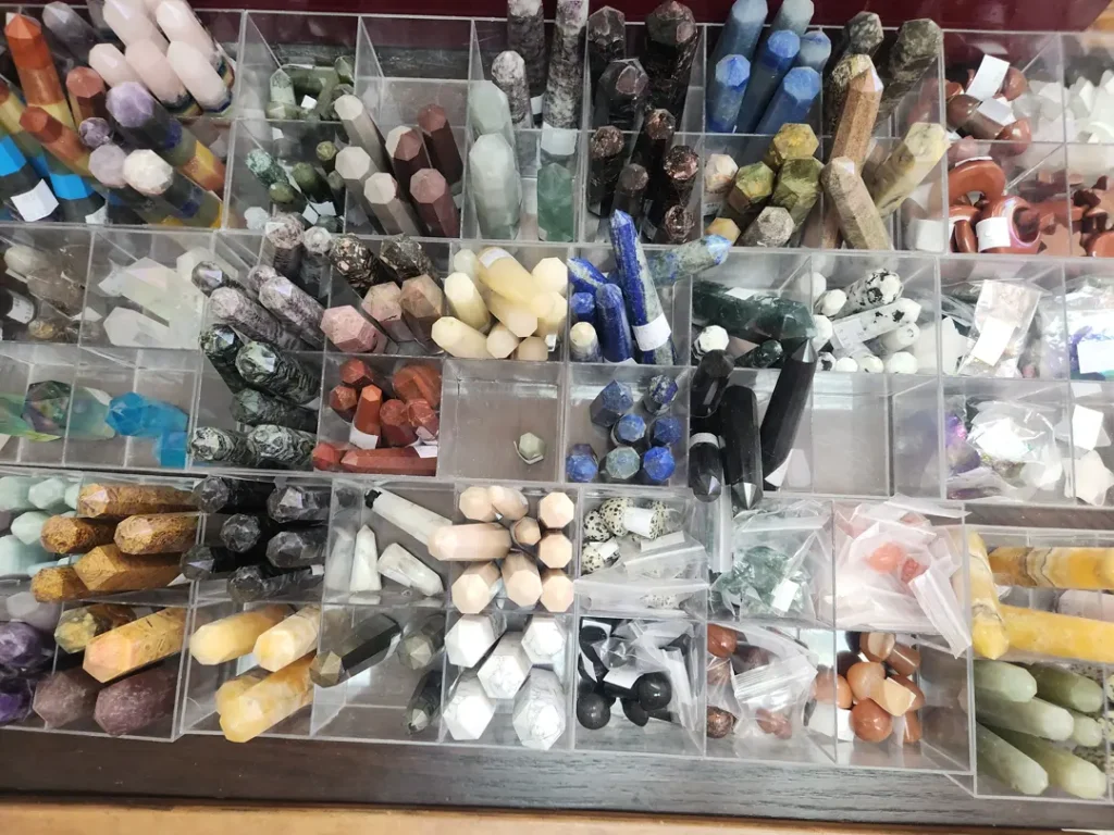Assorted gemstone crystals displayed in various colors and shapes, organized in clear compartments.