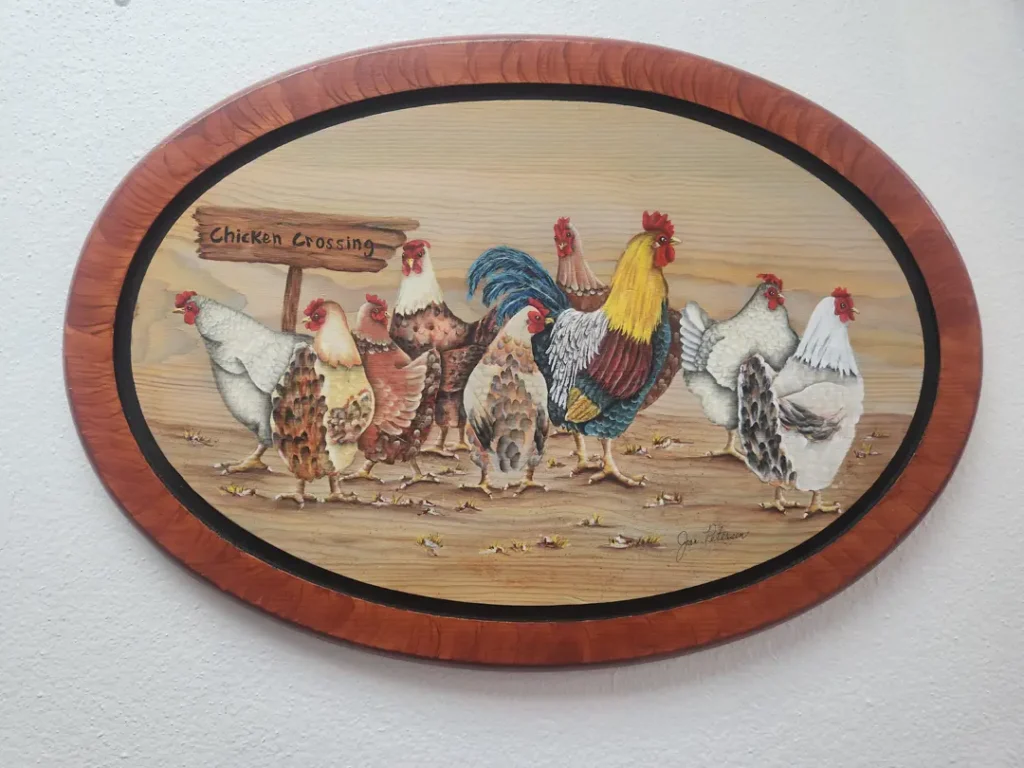 Oval plaque with painted illustration of seven chickens and a rooster walking. Text reads 