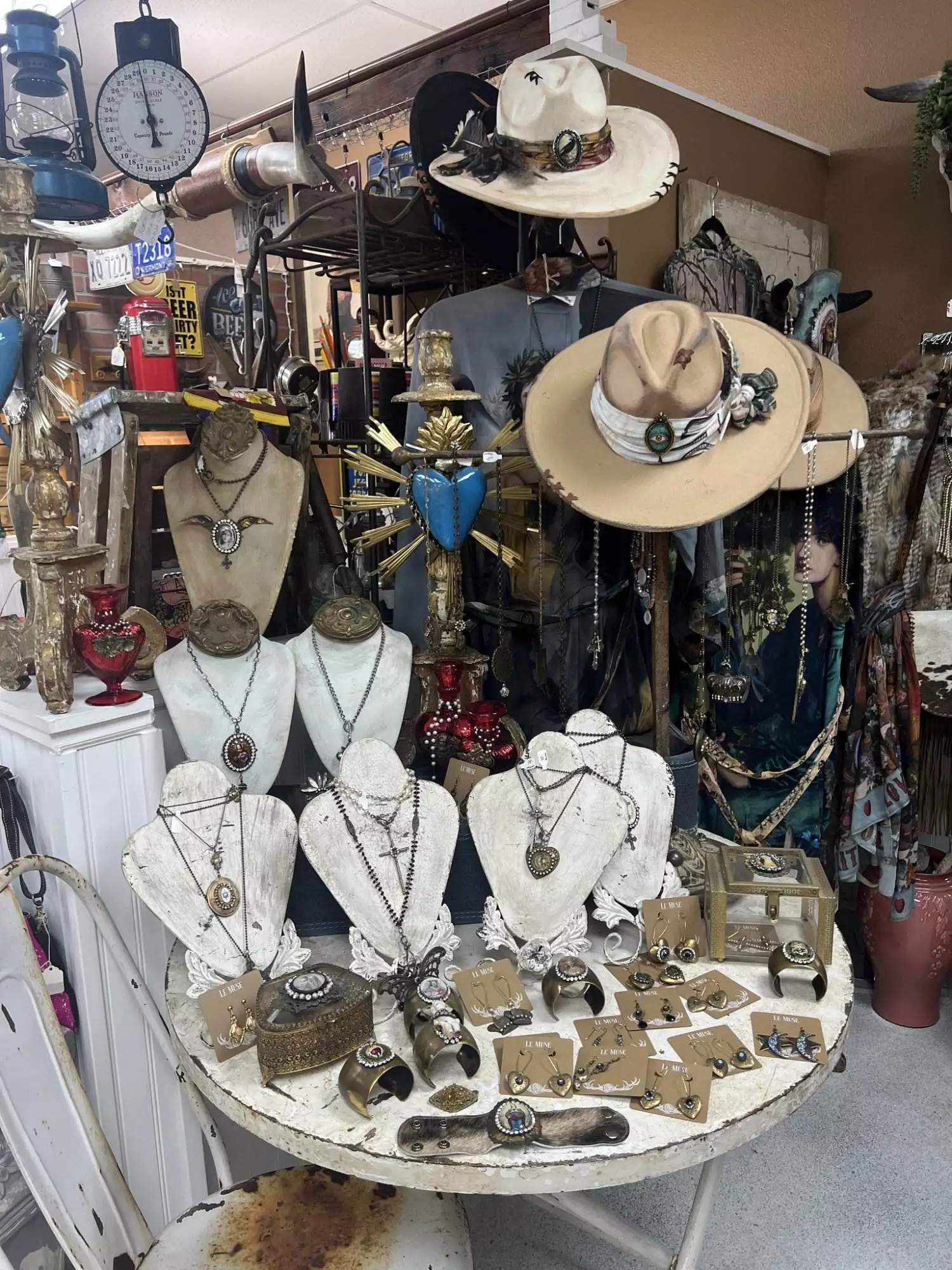 A curated display of vintage accessories, featuring Southwestern necklaces, turquoise rings, and cowboy hats, is artfully arranged on mannequins and a round table at Red Coyote Trading Post in Ft. Mohave, AZ's rustic store setting.