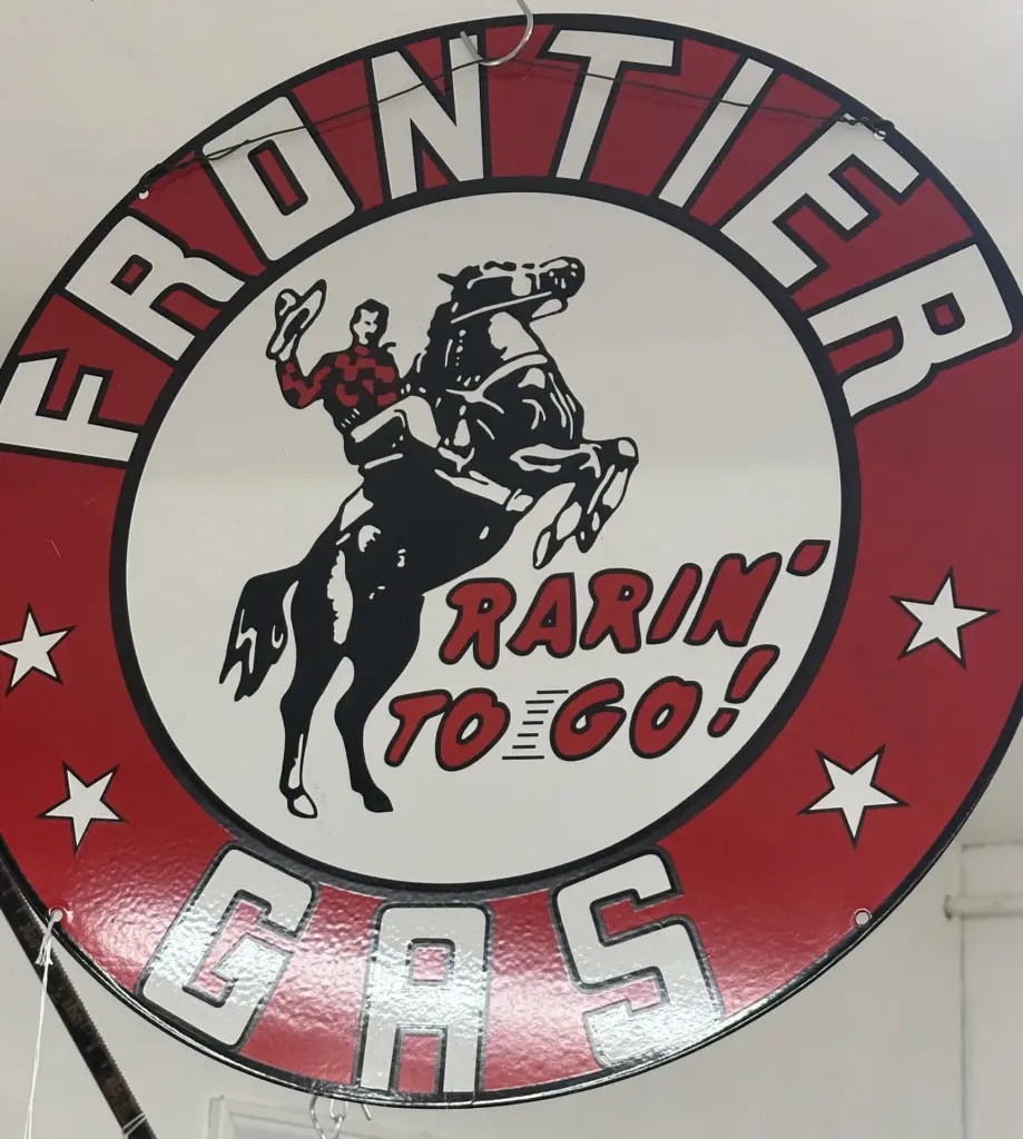 Round red and white Frontier Gas sign showing a cowboy on a rearing horse, with the words Rarin' to go