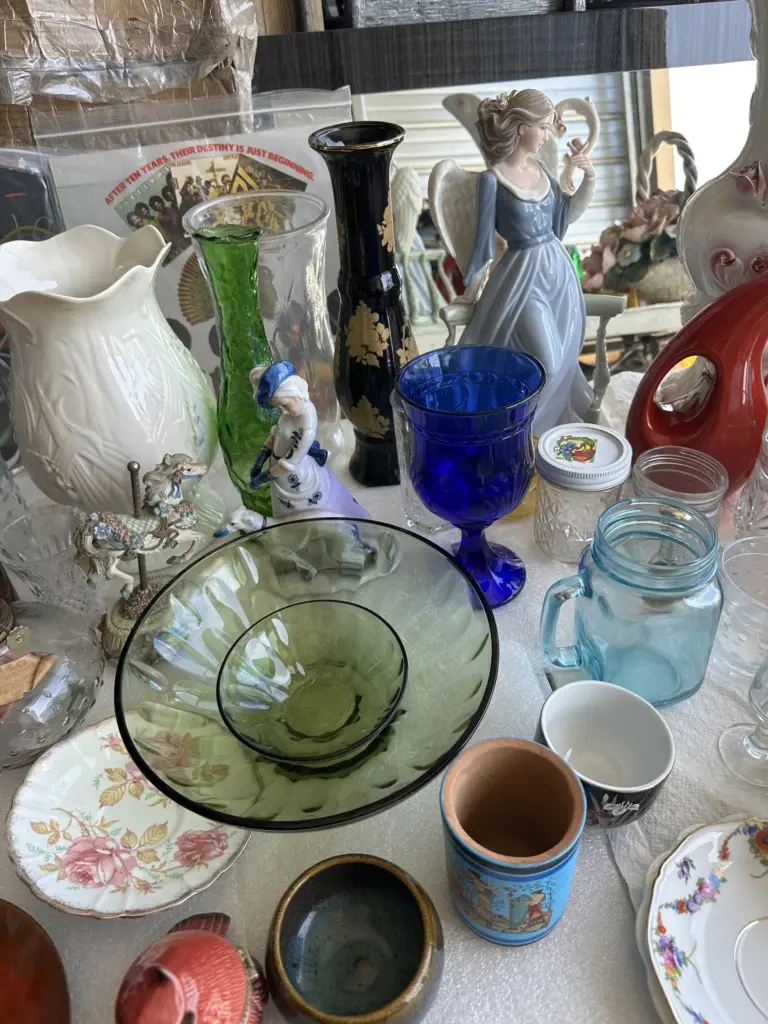 Tabletop of vintage glassware and china: a cobalt blue goblet, green glass bowls, a black and gold vase and a porcelain angel figurine